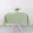 Green tablecloth draped on a white table with a glass and flowers.