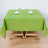 Green tablecloth on a wooden table set for dining with glasses and napkins.