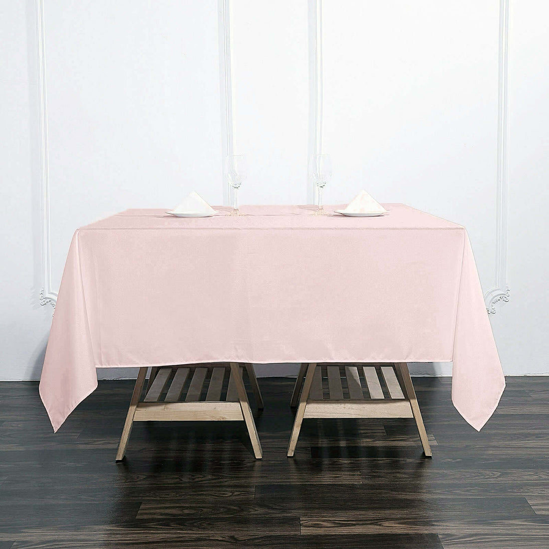 Pink tablecloth draped over a wooden table with folded napkins and glasses.