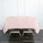 Pink tablecloth draped over a wooden table with folded napkins and glasses.