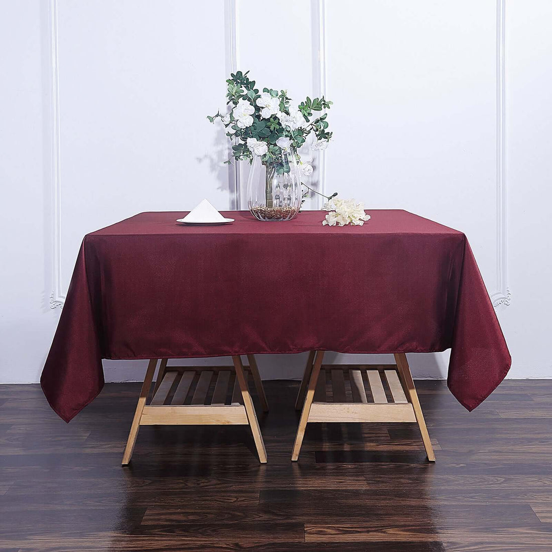 Burgundy tablecloth draped over a wooden table with floral centerpiece.