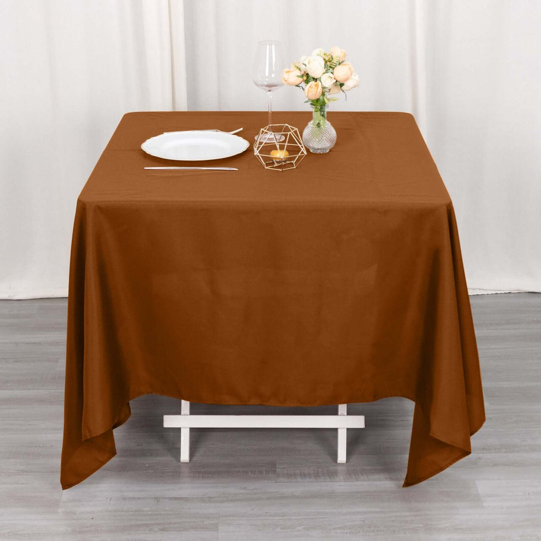 Brown tablecloth draped over a table set with a plate, glass, and flowers.