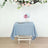 Blue tablecloth on a wooden table with flowers above.