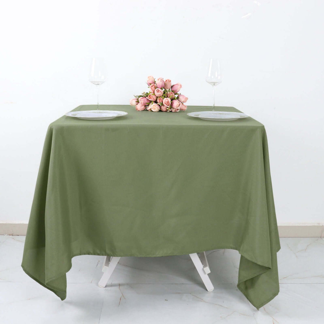 Olive green tablecloth draped over a table with plates and a floral centerpiece.