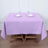Purple tablecloth draped over a wooden table set for two with glasses and cutlery.