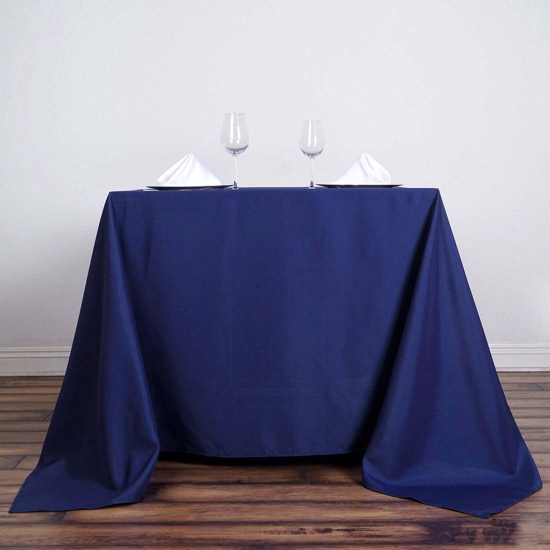 Navy tablecloth draped over a table set for two with glasses and napkins.