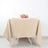 Beige tablecloth on a table set for two with a floral centerpiece.