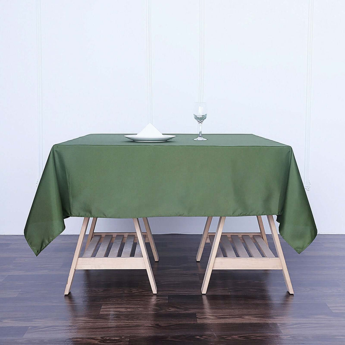 Green tablecloth draped over a wooden table with a plate and glass on top.