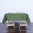 Green tablecloth draped over a wooden table with a plate and glass on top.