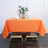 Orange tablecloth on a wooden table with decorative flowers and a napkin.