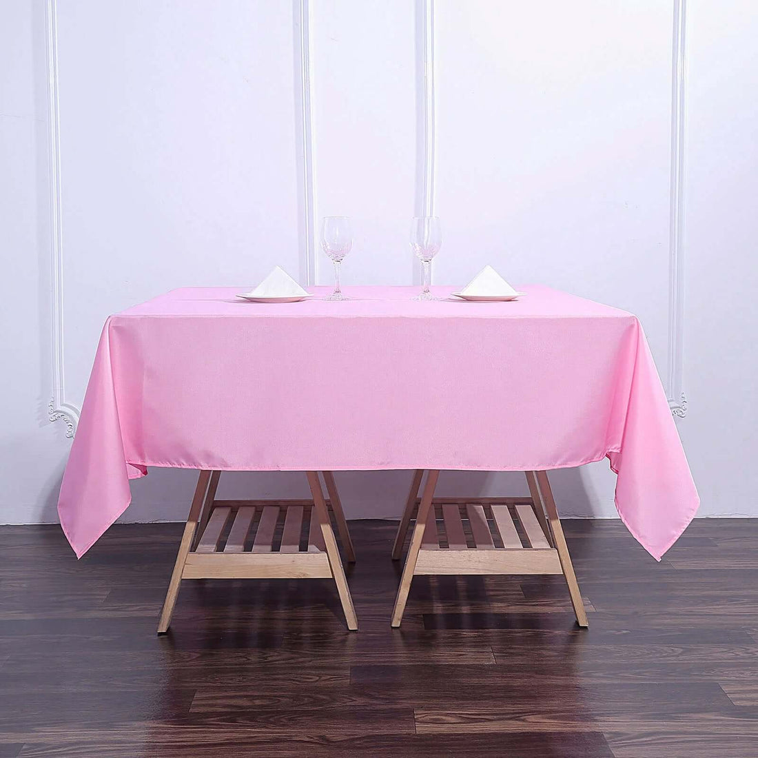 Pink tablecloth on a wooden table set with glasses and napkins.