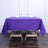Purple tablecloth on a wooden table set with glasses and napkins.