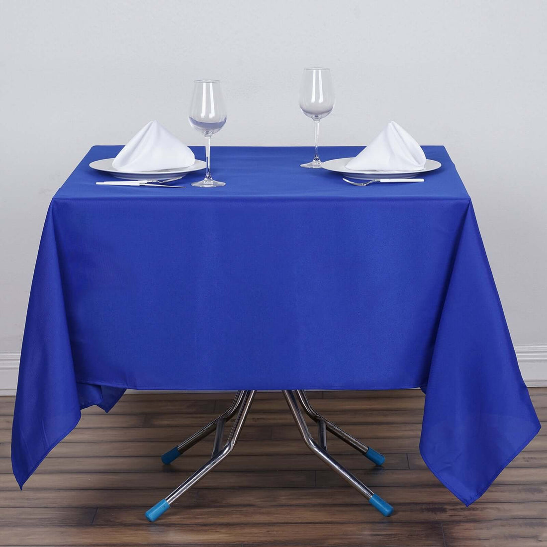 Blue tablecloth set for dining with glasses and napkins on a wooden floor.