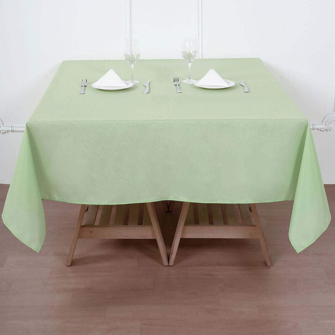 Green tablecloth set on a wooden table with utensils and glassware.