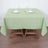 Green tablecloth set on a wooden table with utensils and glassware.