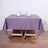 Purple tablecloth draped over a wooden table with plates and glasses on top.