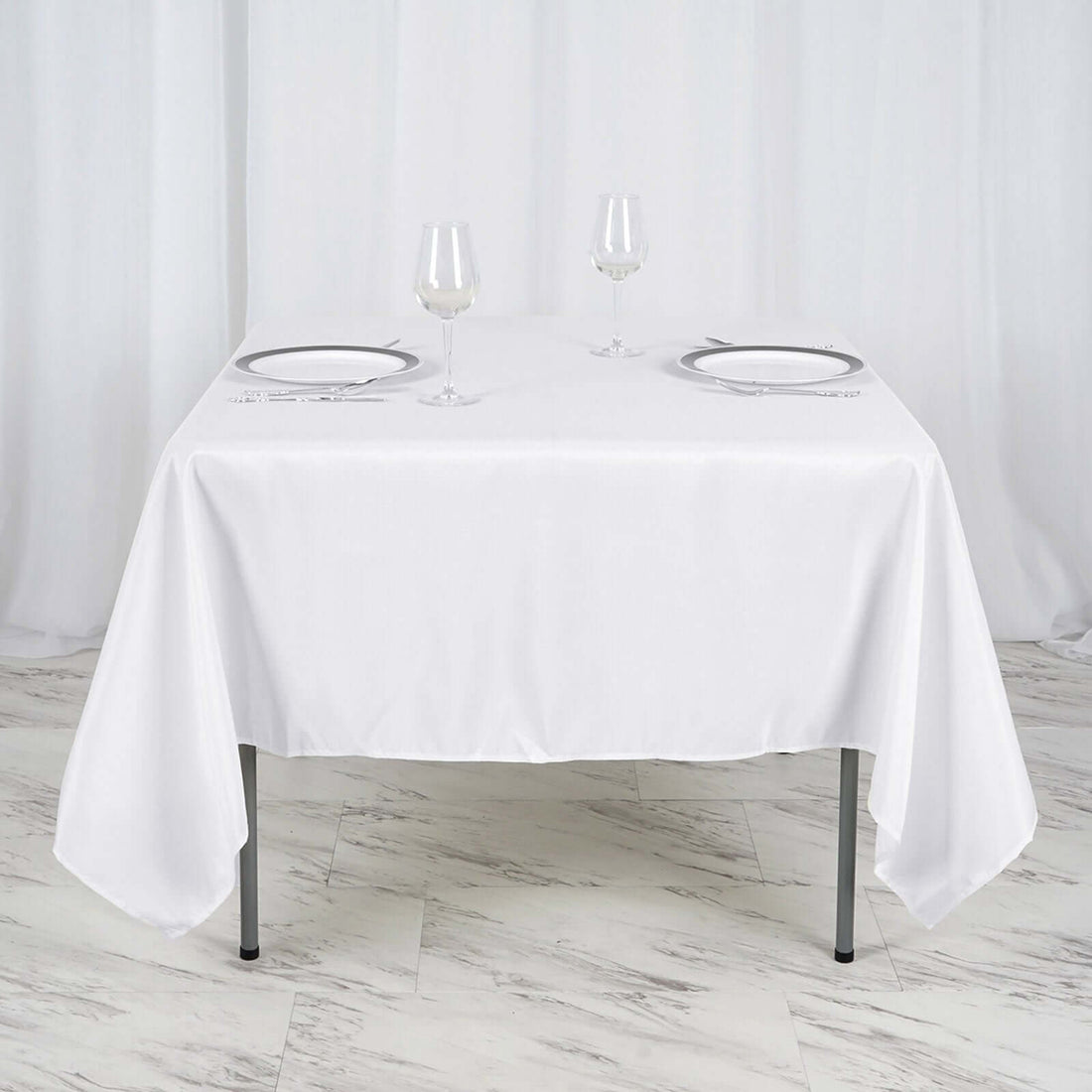 White tablecloth draped over a table set for two with glasses and plates.