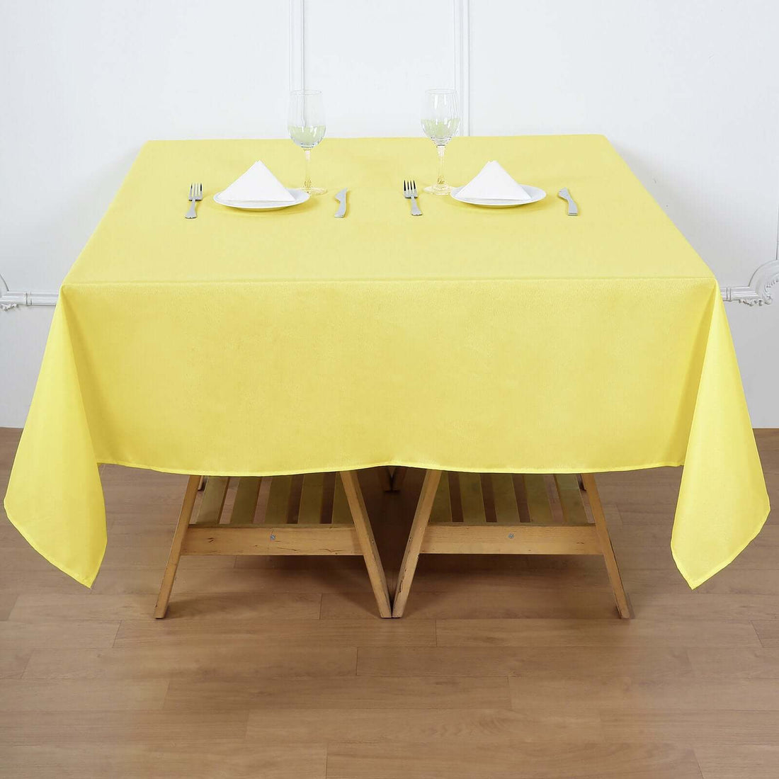 Yellow tablecloth draped over a wooden table set for two with glasses and utensils.