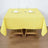 Yellow tablecloth draped over a wooden table set for two with glasses and utensils.