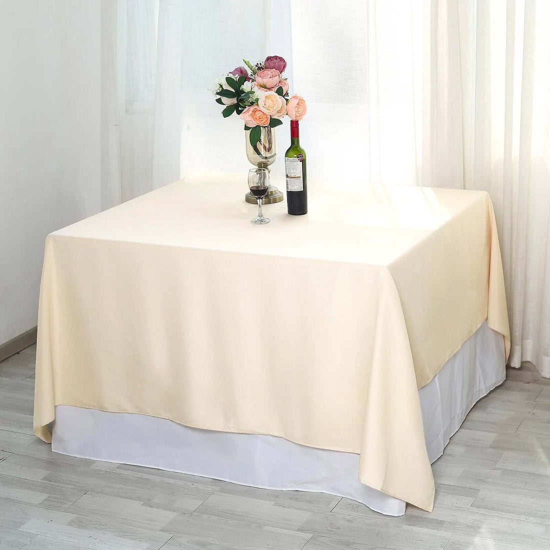 Cream tablecloth draped over a table with a vase of flowers and a wine bottle.