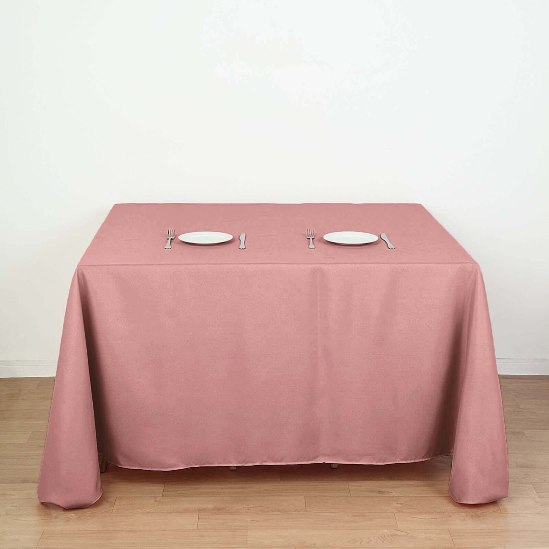 Pink tablecloth draped over a dining table set with plates and utensils.