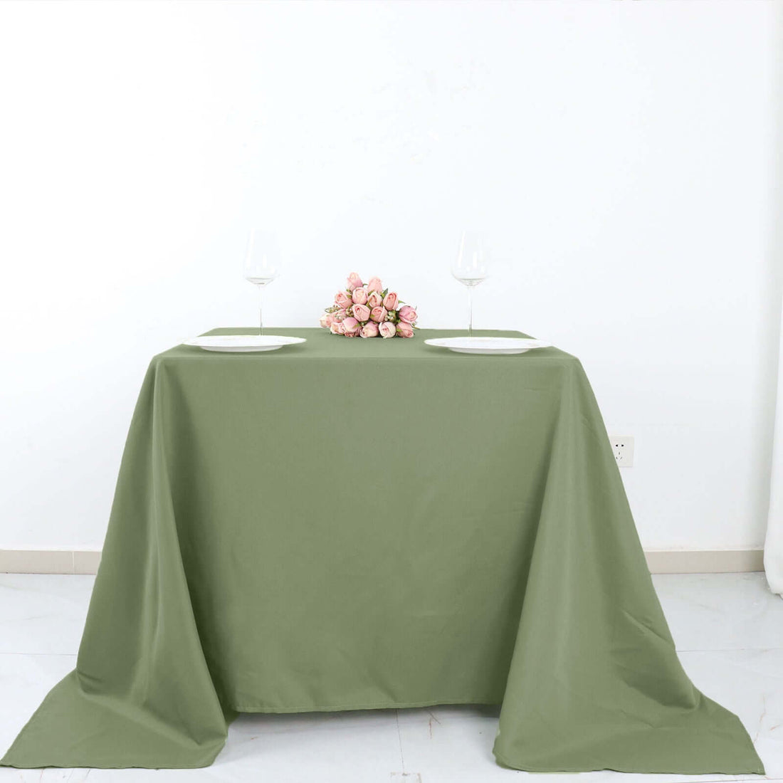 Green tablecloth draped elegantly on a table with plates and a floral centerpiece.