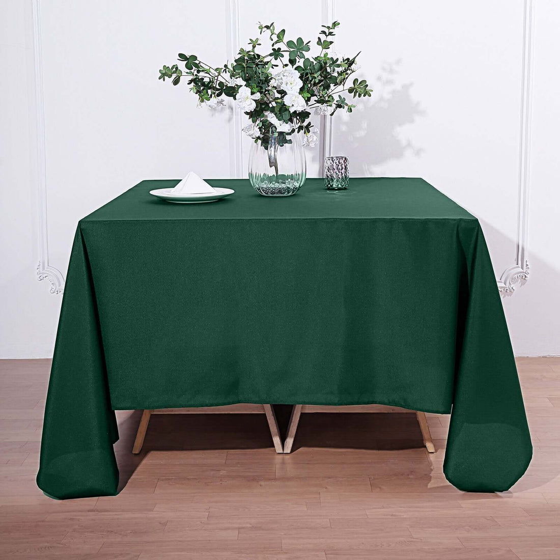 Green tablecloth draped over a wooden table with floral centerpiece.