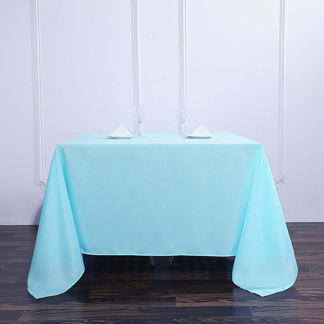 Light blue tablecloth draped over a table with glasses and napkins.