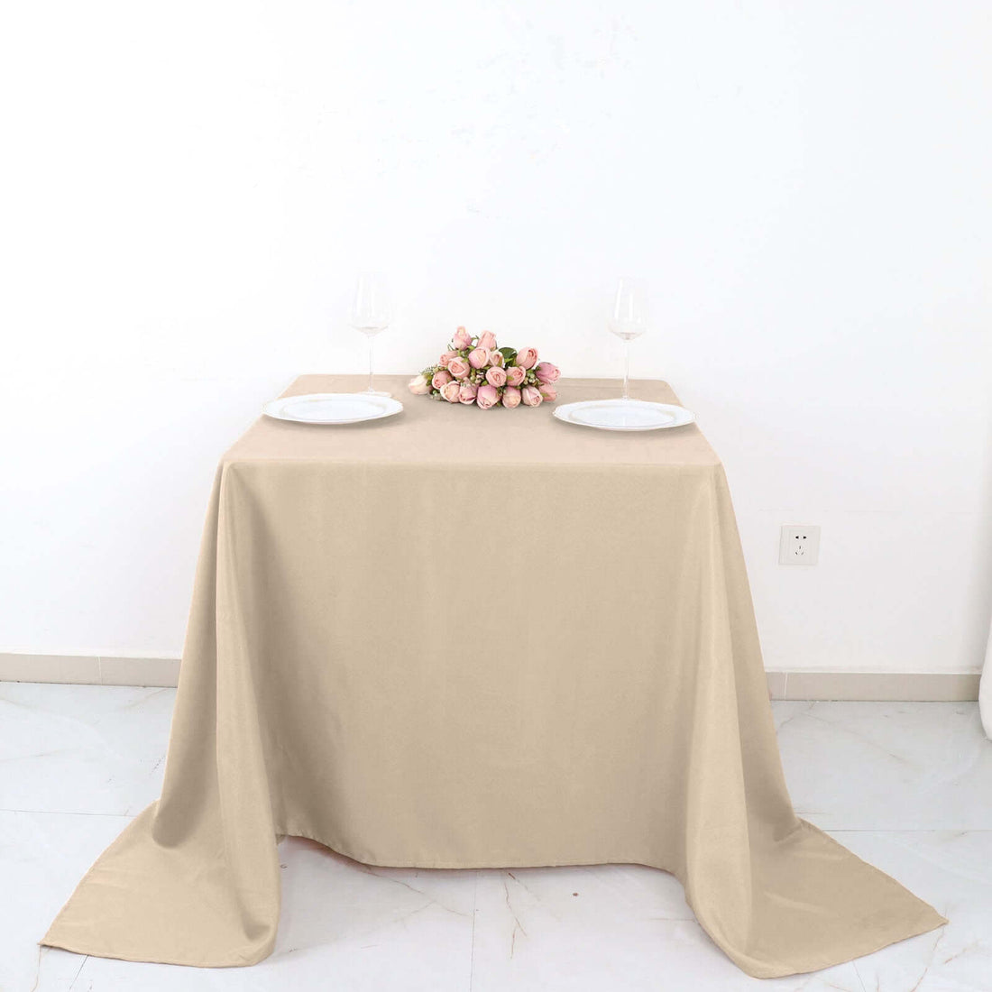 Beige tablecloth draped over a table with plates and a bouquet of roses.