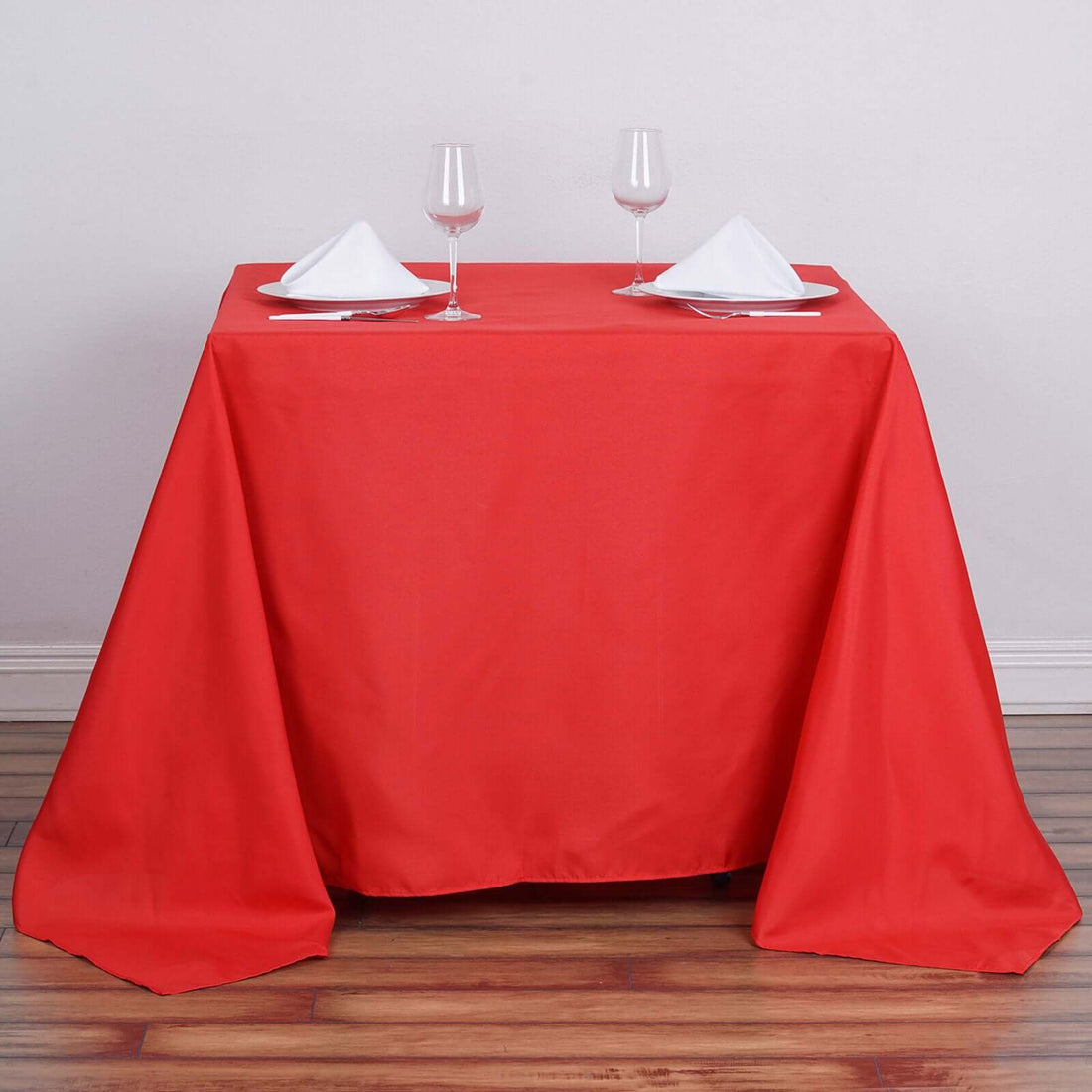 Red tablecloth draped over a table set for two with glasses and napkins.