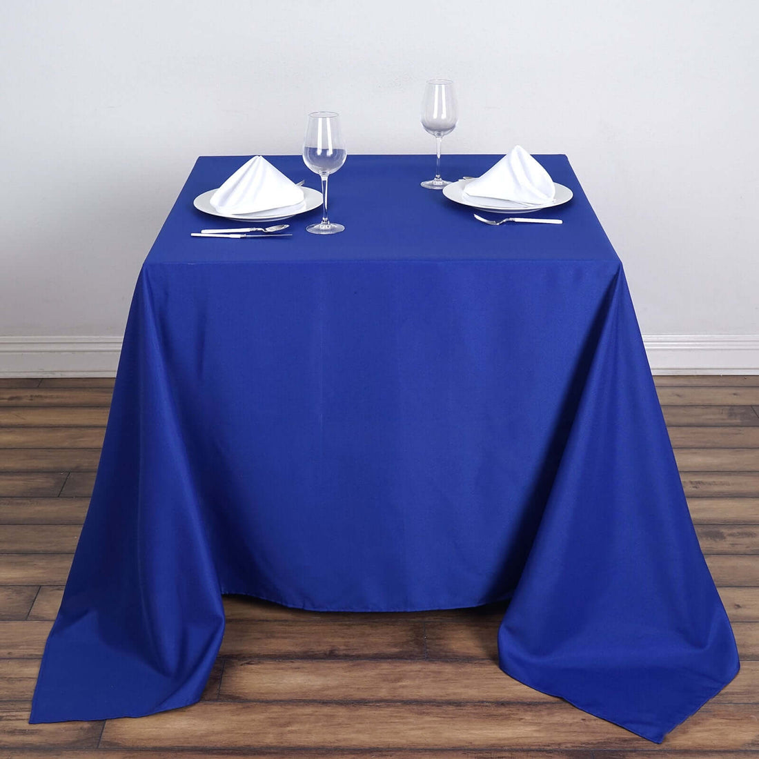 Blue tablecloth draped over a table set for two with glasses and plates.