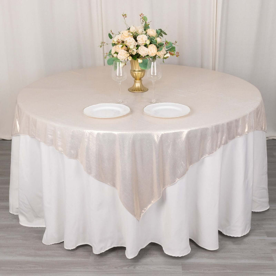 Round table set with a beige tablecloth, plates, and a floral centerpiece.