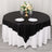 Elegant round table set with black and white tablecloth, floral centerpiece, and dinnerware.
