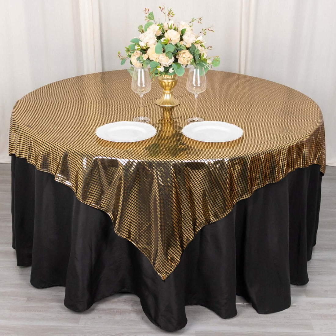 Round table with gold sequin tablecloth, black skirt, and floral centerpiece.