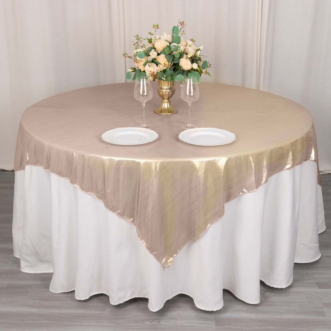 Elegant round table set with beige tablecloth, floral centerpiece, and dinnerware.