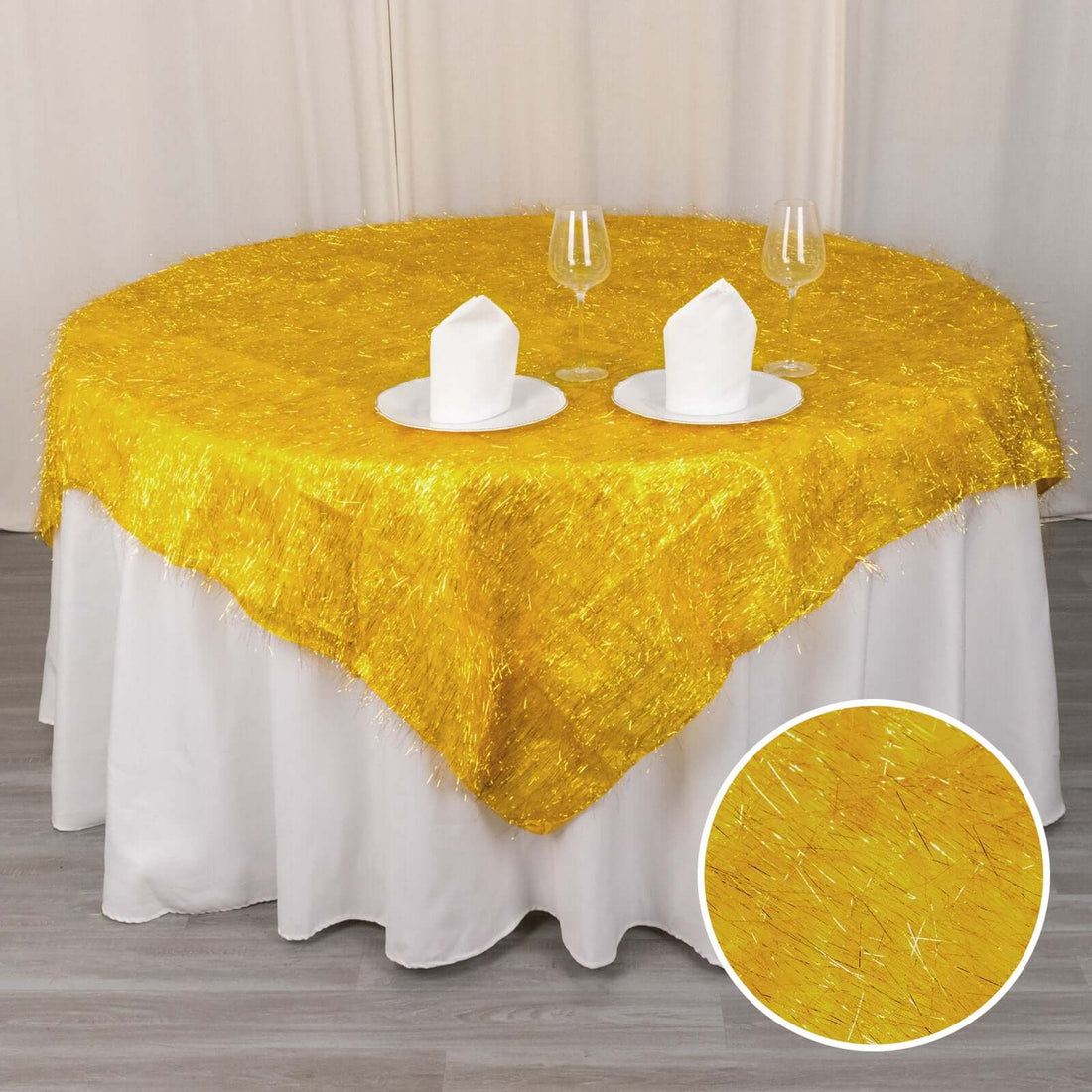 Yellow decorative tablecloth with shiny fringes on a round table setting.