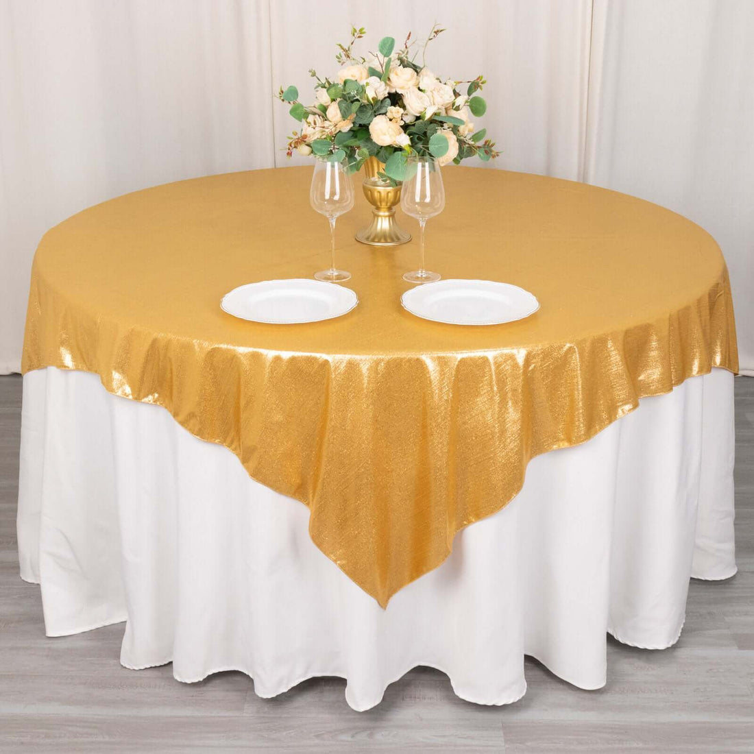 Gold tablecloth with elegant floral centerpiece and dinnerware on a round table.