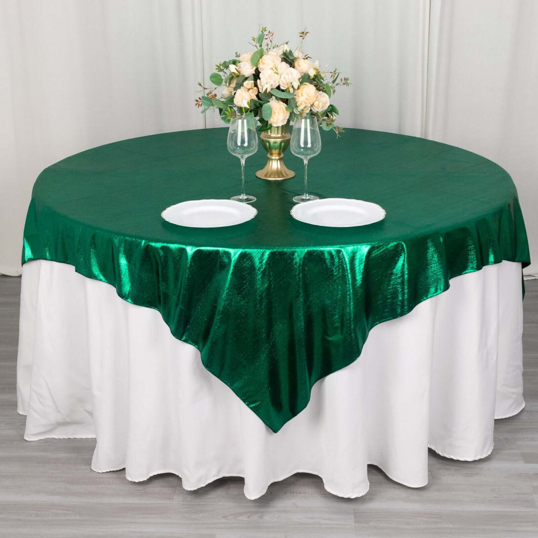 Round green tablecloth with white draping, set for dining with floral centerpiece.