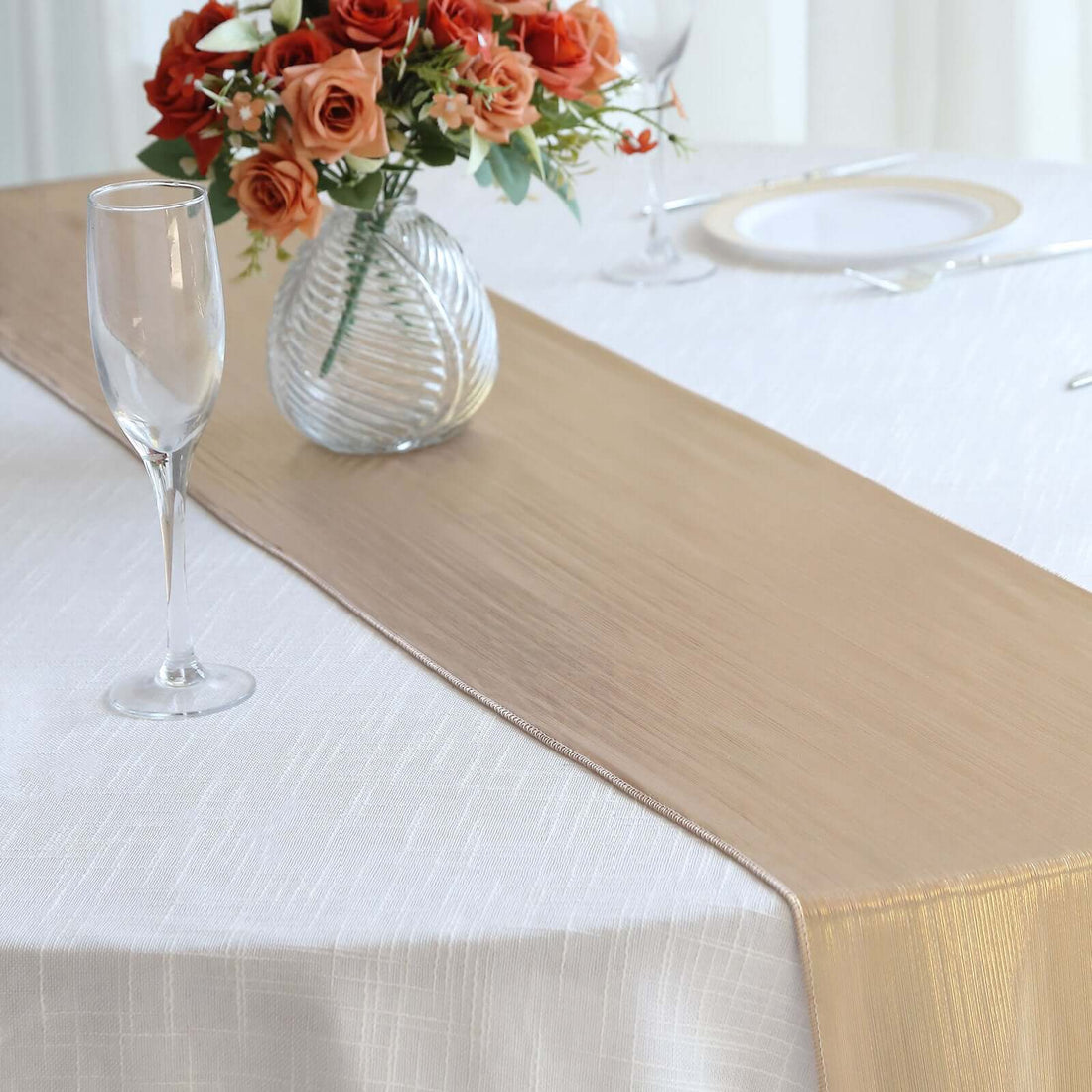 Elegant gold table runner on a white table with floral centerpiece.