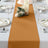 Table runner in warm gold color, styled with candles and floral decor on a dining table.