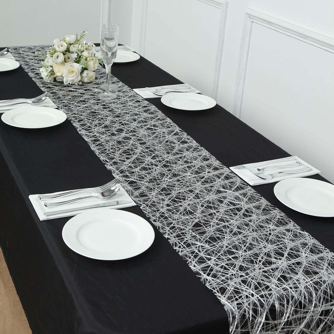 Elegant black table setting with a decorative silver table runner and white plates.