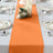 Orange table runner on a set dining table with plates and decorative candles.