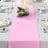 Pink table runner on a dining table set with plates, glasses, and candles.