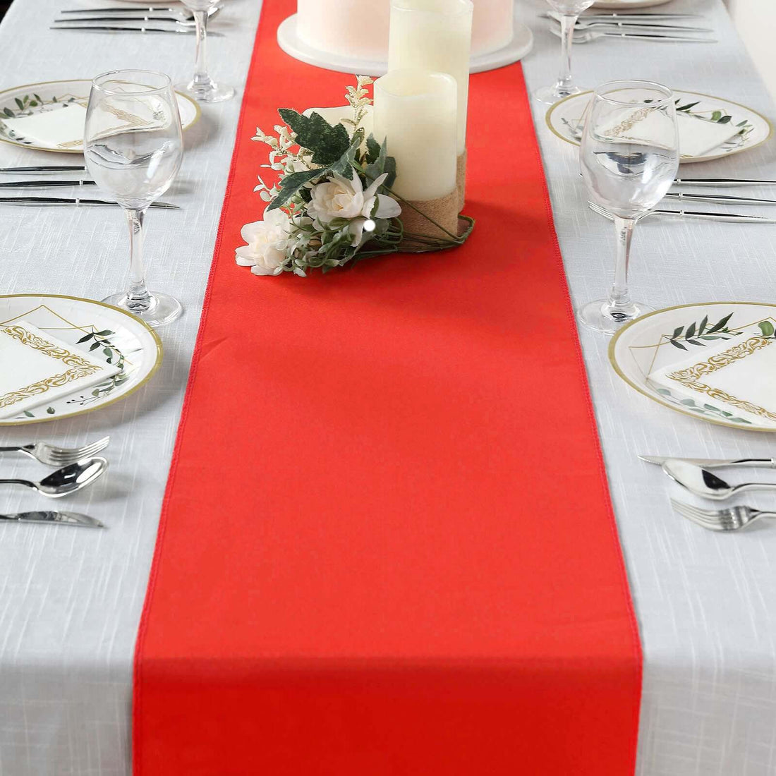 Red table runner on a dining table set with plates and decorative candles.
