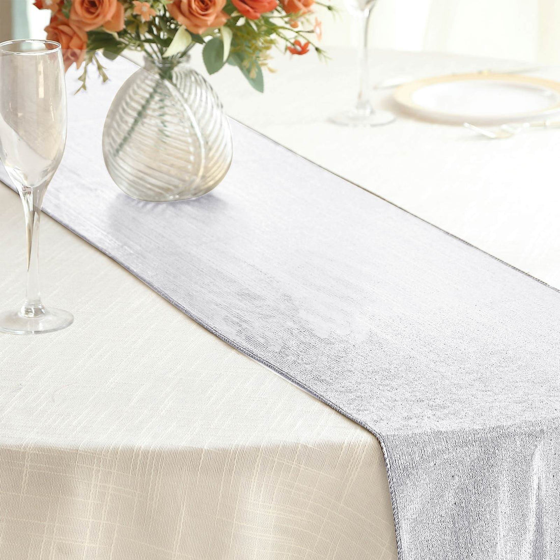 Silver table runner on a dining table with floral centerpiece.