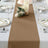 Brown table runner on a beautifully set dining table with candles and floral decor.