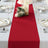 Red table runner on a dining table set with plates and candles.