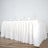 White table with a pleated skirt and glasses on top, set against a plain backdrop.