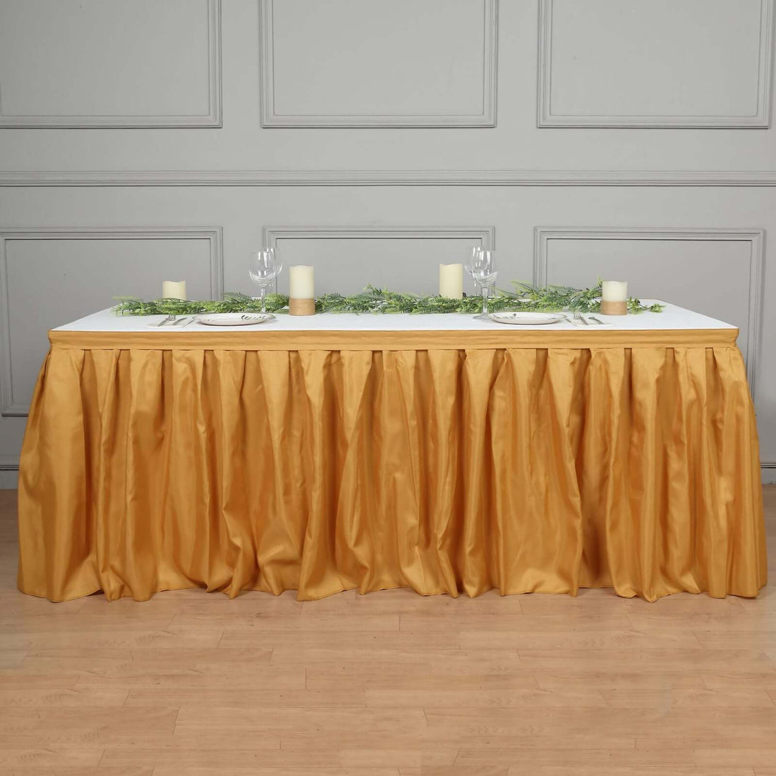 Elegant gold table skirt draped over a white table with candles and greenery decoration.