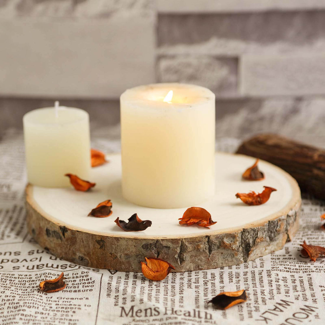 Candle on a wooden slice with dried petals on newspaper background.